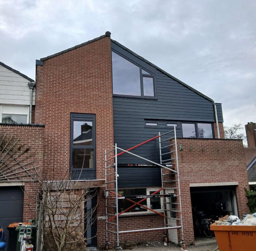 Gevelrenovatie met nieuwe kozijnen en donkergrijze gevelbekleding (steiger zichtbaar)